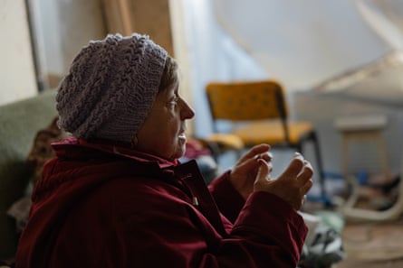Elderly Ukrainian woman in woolly hat and coat sitting in her apartment