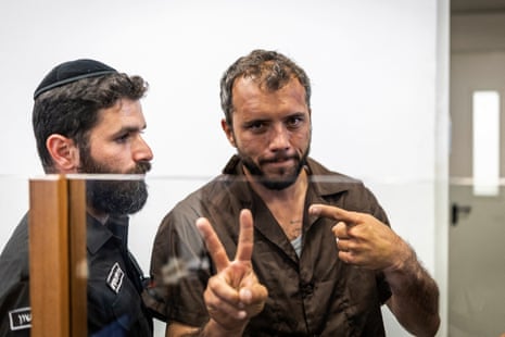 Brazilian activist Thiago Avila makes a peace sign in court as an Israeli officer stands next to him.