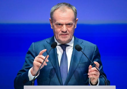 Close up of Donald Tusk at the podium gesturing with both hands, looking serious