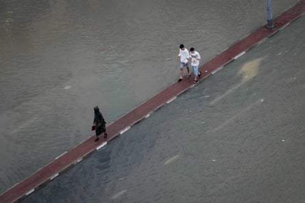 Pedestrians walk on a road divider along a flooded street in the United Arab Emirates.