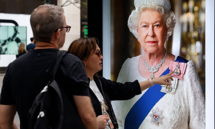 Members of the public in front of an image of late Queen Elizabeth II, on a bus stop on Oxford Street in London.