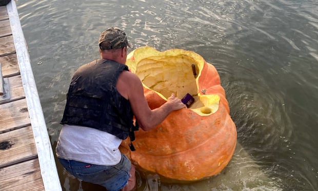 man in lifejacket holds on to giant pumpkin near dock