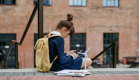 A girl with a backpack on sits on steps and looks at her smartphone.