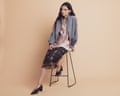 A model sitting ona stool wearing a dark patterned midi skirt, a lacy camisole and a grey jacket