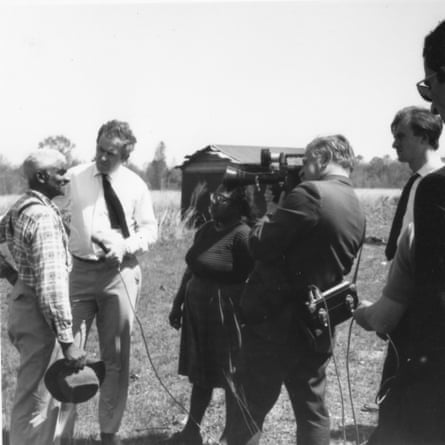 Black and white photo of a man being interviewed by two people, one holding a microphone, the other a camera