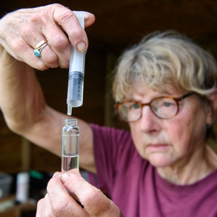 Anne Cottringer, in a T-shirt and glasses, squeezes water from a syringe into a glass vial