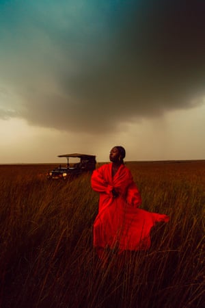 A woman in a field with clouds above and a vehicle in the background