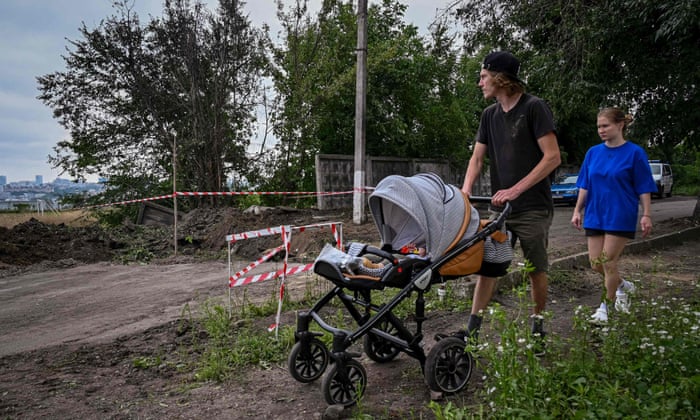 UKRAINE-RUSSIA-CONFLICT-WARA family pushes a baby carriage past a crater after a missile strike on the second largest Ukrainian city of Kharkiv on August 3, 2022, as the Russia-Ukraine war enters its 160th day. (Photo by SERGEY BOBOK / AFP) (Photo by SERGEY BOBOK/AFP via Getty Images)