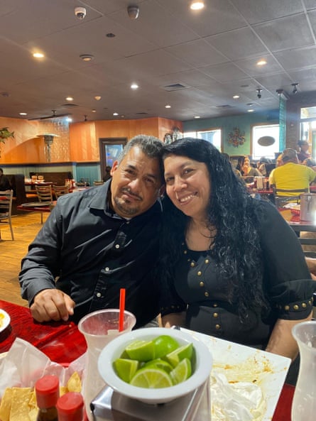 A middle-aged man and woman smile in front of a table loaded with food in a restaurant.