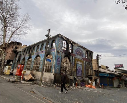 The fire-damaged remains of a rectangular building with high arched windows and covered in ornate blue tile work.