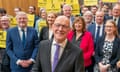 John Swinney smiles for a photograph with a large group of supporters behind him, many of whom are holding yellow "John Swinney" supporter placards