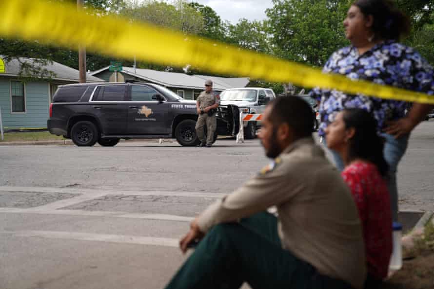 People sit on the curb outside of Robb elementary school as state troopers guard the area in Uvalde, Texas.