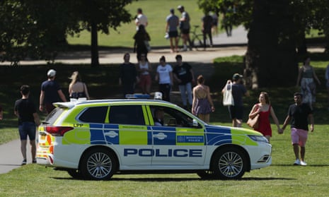 Police officers in a patrol car keep people moving in Greenwich Park, London