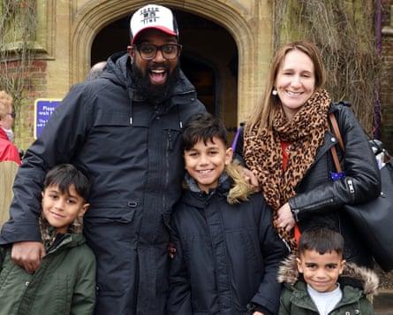 Romesh Ranganathan and his family stand in a close group, smiling at the camera