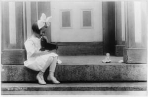 black and white photo of a young girl sitting on stoop taking photo of doll