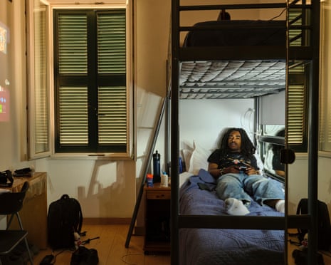 Stevie lies on a bunk bed holding a game controller in his dimly lit Rome bedroom
