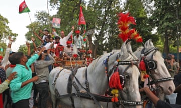 People waving flags stand on a carriage pulled by horses