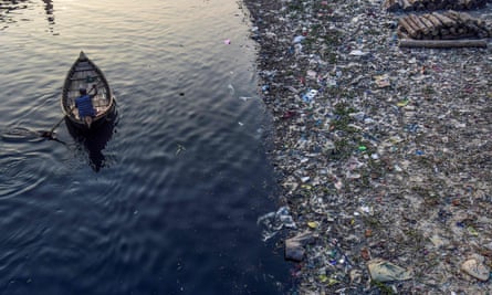 A man paddles on a boat as plastic bags float on the water surface of the Buriganga river in Dhaka.