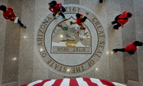 people in red shirts walk over a stone floor with a crest and writing that says great seal of the state of arizona