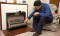 An elderly man sitting in his front room with his hat and scarf on warming his hand against his electric fire.<br>D2BMGN An elderly man sitting in his front room with his hat and scarf on warming his hand against his electric fire.