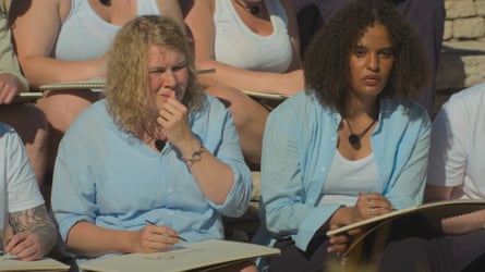 Two young women wearing blue shirts, and row of women in white vests behind them