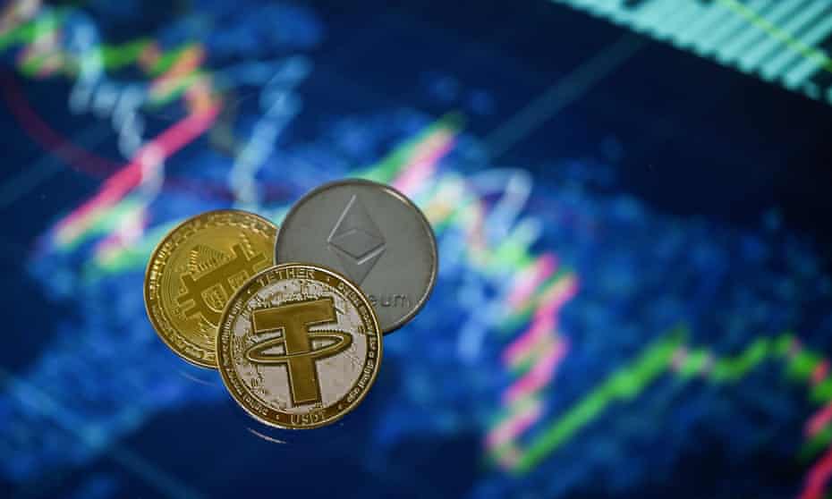 Gold plated souvenir cryptocurrency Tether (USDT), Bitcoin and Etherium coins arranged beside a screen displaying a trading chart.