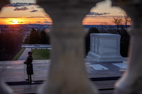 A soldier, photographer between a row of columns, standing guard at the tomb of the unknown solider at sunrise.