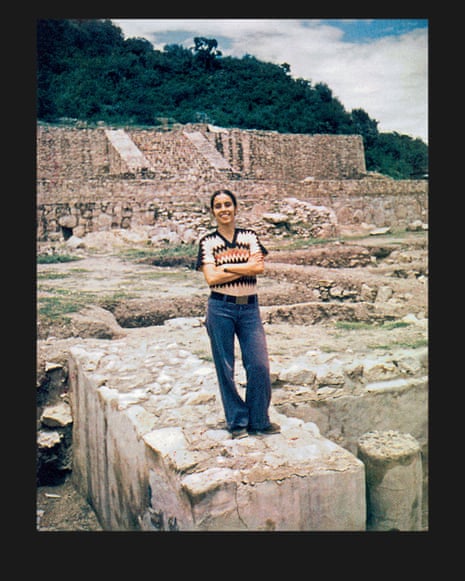 A woman standing on rocks wearing jeans, with her arms folded and smiling.