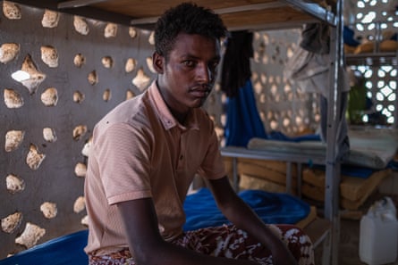 A young man sits on a bunk-bed.