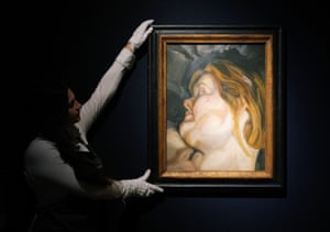 A spotlight in a darkened room falls on a painting held by a woman in a white shirt and wearing white gloves in the shadows