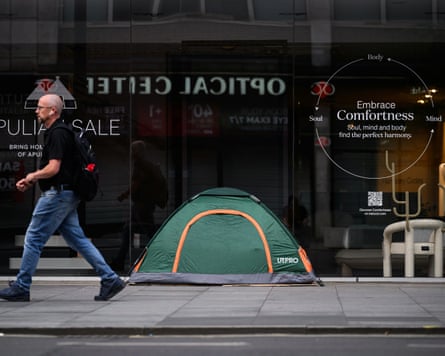 A man walks past a homeless person’s tent pitched on a London pavement