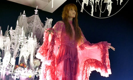 Florence Welch in pink gown in front of cobweb-heavy chandeliers.