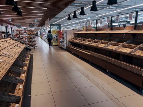 A shopper walks past rows of empty shelves in an Italian supermarket aisle