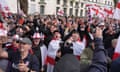 People wave flags during a St George's Day rally on Whitehall, in Westminster, central London, Tuesday 23 April 2024: small crowd, mostly men, some shouting; one is filming a selfie, another is drinking from a bottle of beer, some are wearing red and white hats and have flags draped around their shoulders; they look rowdy but not particularly threatening in this photo