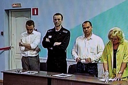 Navalny stands behind a desk with two men and a woman beside him