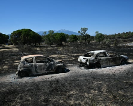 Two burned out cars in a field where the ground is scorched from fire