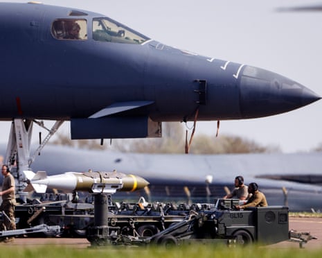 US Air Force personnel prepare a JDAM munition beside a B-1 Lancer bomber on a runway