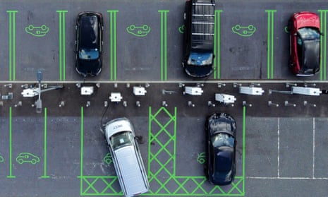 Overhead view of electric vehicles parked within green painted lines while plugged into charging points