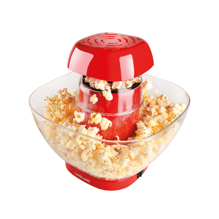 A red popcorn maker sits in a clear bowl overflowing with freshly popped popcorn