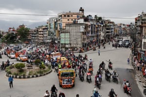A procession featuring large vans and motorbikes moves through the streets