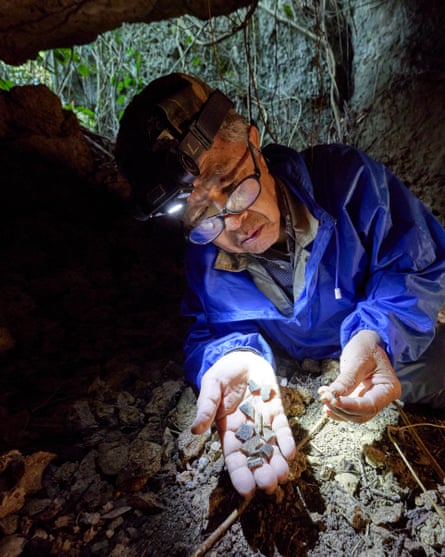 Takamatsu Gushiken inside a cave wearing a head torch illuminating bone fragments on his open palm