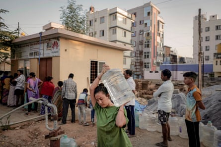 A woman carries a jar of drinking water as people queue at a water vending stall, which extracts and filters borewell water and sells twenty litres of water for five Indian rupees, in Bengaluru, which is facing water shortages, in India, April 25, 2024.