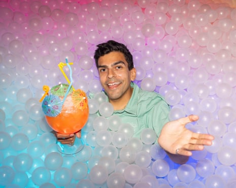 Ammar's head and hands poke out from a sea of clear plastic balls; he holds a huge cocktail with three umbrellas