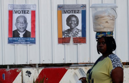 A vendor carrying a bucket on her head walks past campaign posters