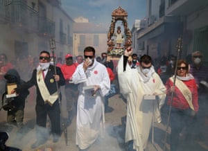 Smoke billows around a group of people in long robes and old-fashioned suits at the front of a procession