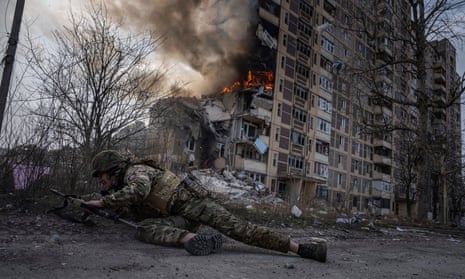 A Ukrainian police officer takes cover in front of a burning building that was hit in a Russian airstrike in Avdiivka.