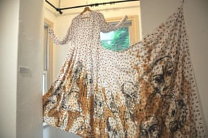Long-sleeved dress with wide, stained skirt is displayed hanging from a curtain rail