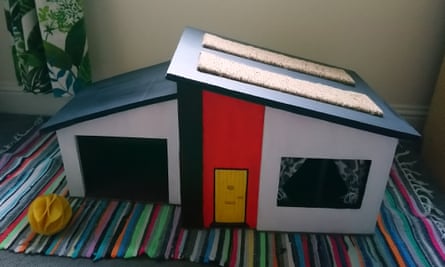 A single-storey model house with a red door and carpet cat scratchers on its sloping roof 