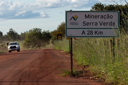 A sign on a red dirt road says ‘Mineração Serra Verde, A 28 km’