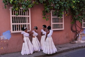 Women in long dresses chatting on a pavement outside an ochre-coloured house